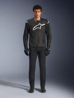 Casaco Alpinestars T-GP Air, casaco de motociclismo têxtil preto com um grande logótipo Astars branco no peito, usado por um modelo com calças de condução e luvas pretas, apresentando painéis perfurados e ventilação em malha para condução desportiva.