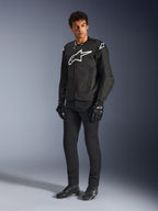 Casaco Alpinestars T-GP Air, casaco de motociclismo têxtil preto, usado por um modelo com calças e luvas pretas a condizer, com um logótipo Alpinestars branco proeminente no peito e nos ombros, painéis de malha ventilados e um corte desportivo derivado da competição.
