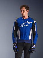 Alpinestars T-GP Air Jacket, casaco de motociclismo têxtil desportivo, azul vivo e azul-marinho com detalhes brancos, logótipo de estrela grande no peito, painéis de ventilação em malha, usado por modelo com luvas a condizer e calças pretas