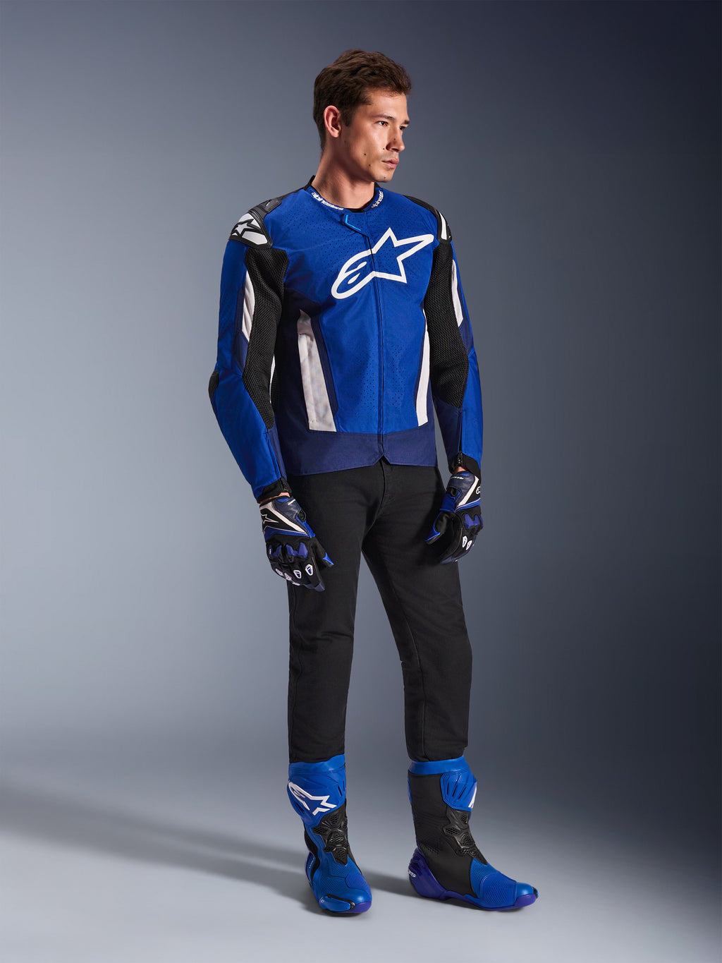 Casaco Alpinestars T-GP Air, casaco de motociclismo têxtil desportivo, azul brilhante, azul-marinho e branco, usado com luvas azuis e pretas a condizer, calças pretas e botas de corrida azuis, com logótipo branco no peito e painéis de malha técnica, fotografia de estúdio de corpo inteiro