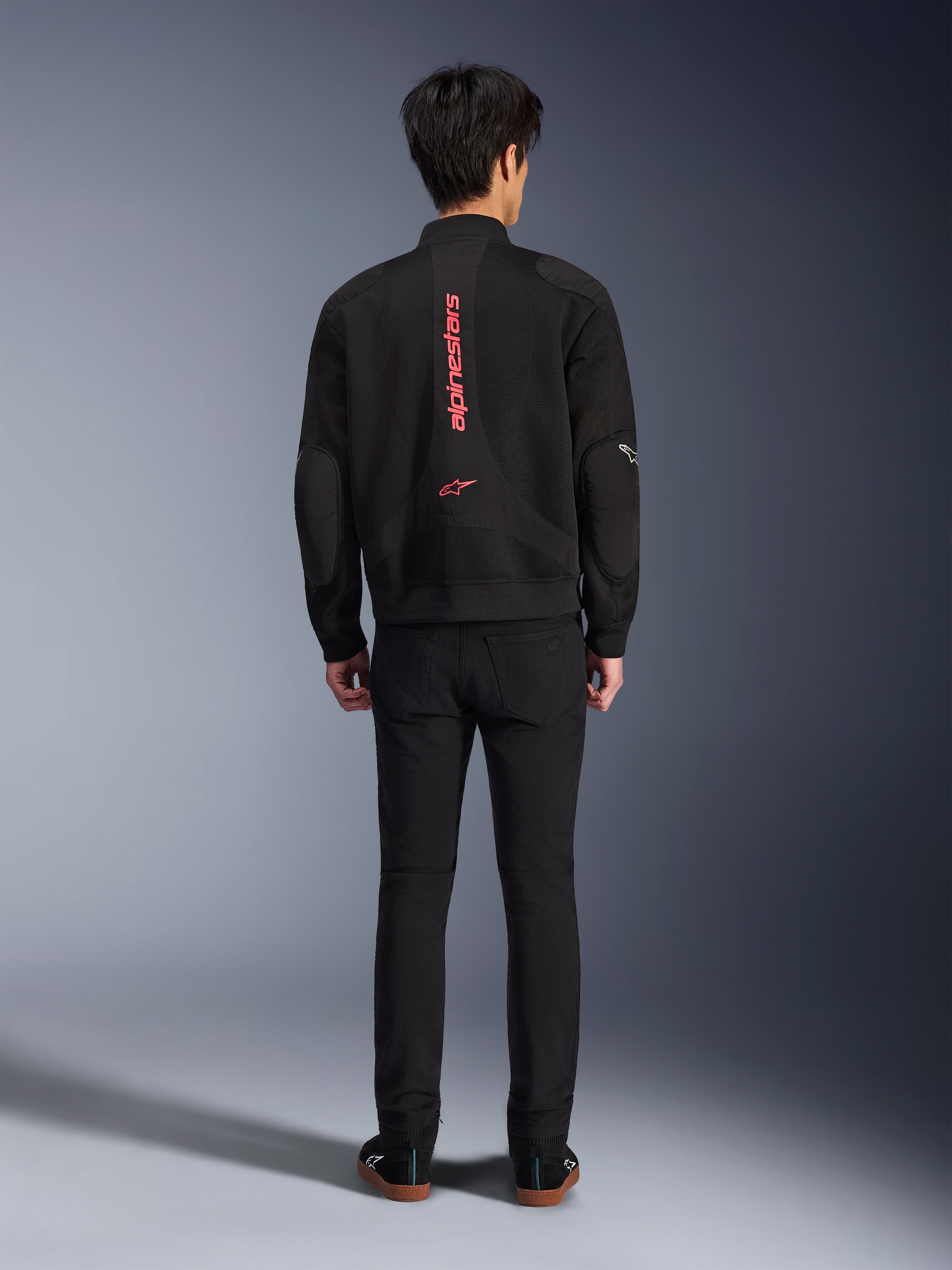 Alpinestars Flight Air Jacket in Black Bright Red, Rear view of urban bomber-style motorcycle jacket, featuring vertical red Alpinestars branding and logo on the spine, lightweight 3D mesh construction, worn with black pants for a contemporary look.