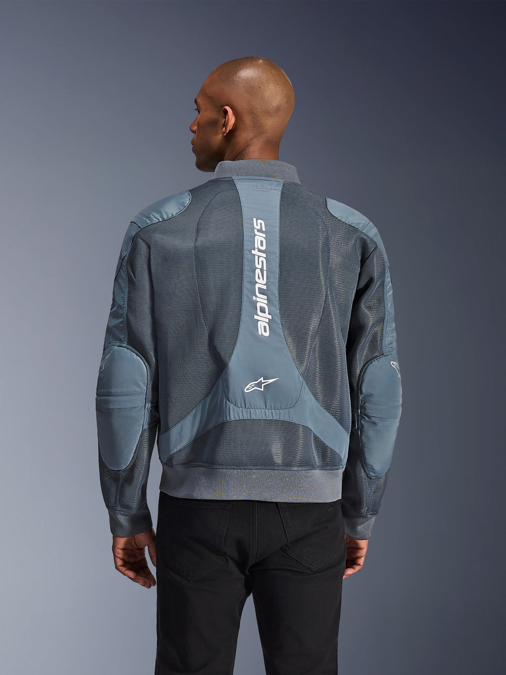 Alpinestars Flight Air Jacket em Storm Gray, vista traseira num modelo, casaco de motociclismo urbano com painéis de malha 3D alargados, marca Alpinestars vertical nas costas, gola e bainha caneladas de estilo bomber