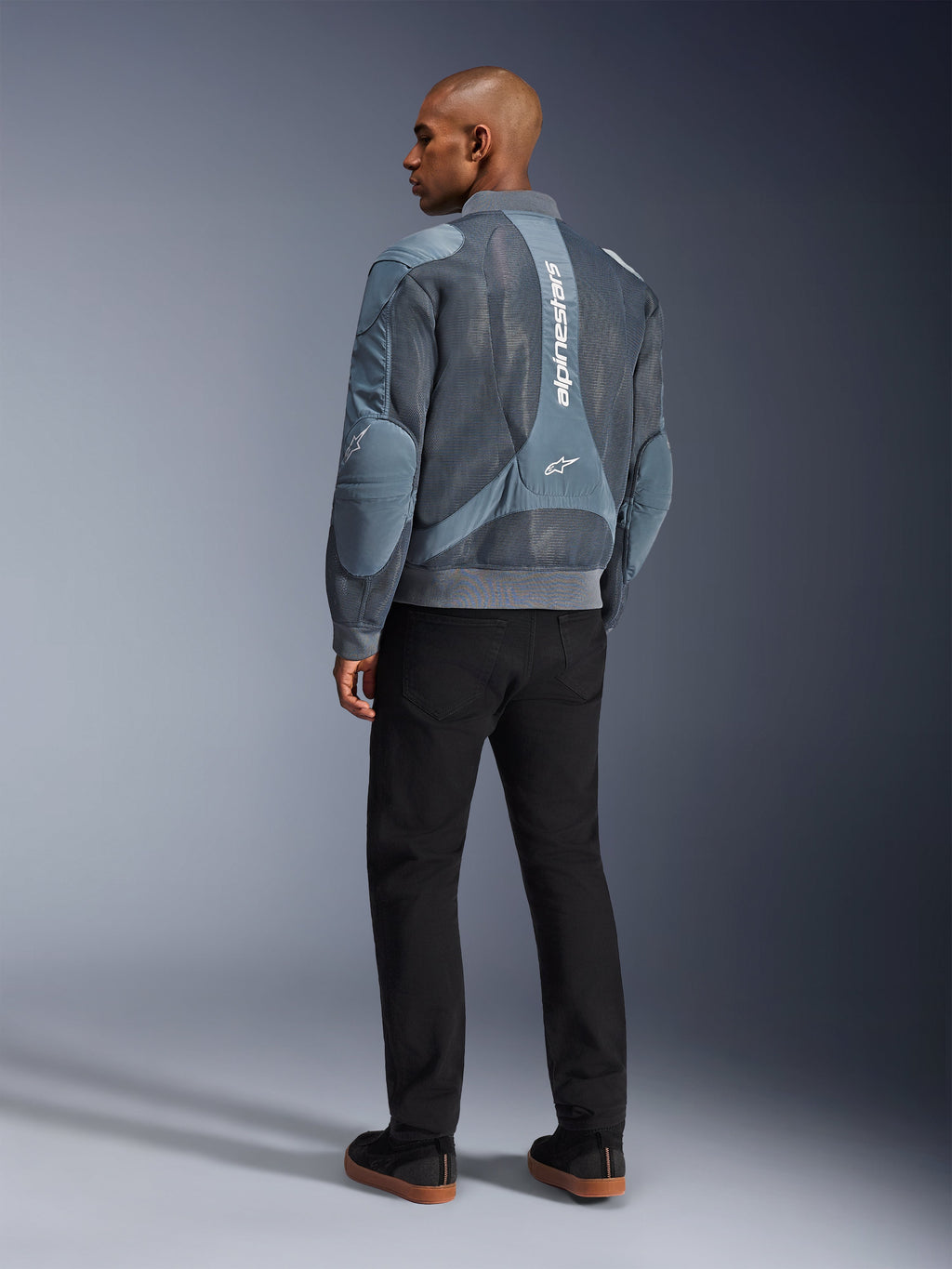 Casaco Alpinestars Flight Air, casaco de motociclismo Storm Gray, vista traseira, com painéis de ventilação em malha 3D e marca Alpinestars branca vertical, usado com calças pretas e ténis pretos, estilo urban commuter