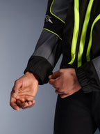 Casaco Alpinestars Unite, casaco de motociclismo urbano, preto e asfalto com detalhes em amarelo néon, grande plano das mãos a ajustar o punho elastizado da manga, equipamento de proteção minimalista inspirado em streetwear