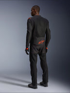 Male rider from the back wearing the Alpinestars Viper Air V4 Jacket, Black and Red Fluo, featuring an orange Astars logo on the lower back and shoulders, mesh textile construction, styled with matching black motorcycle pants and boots.