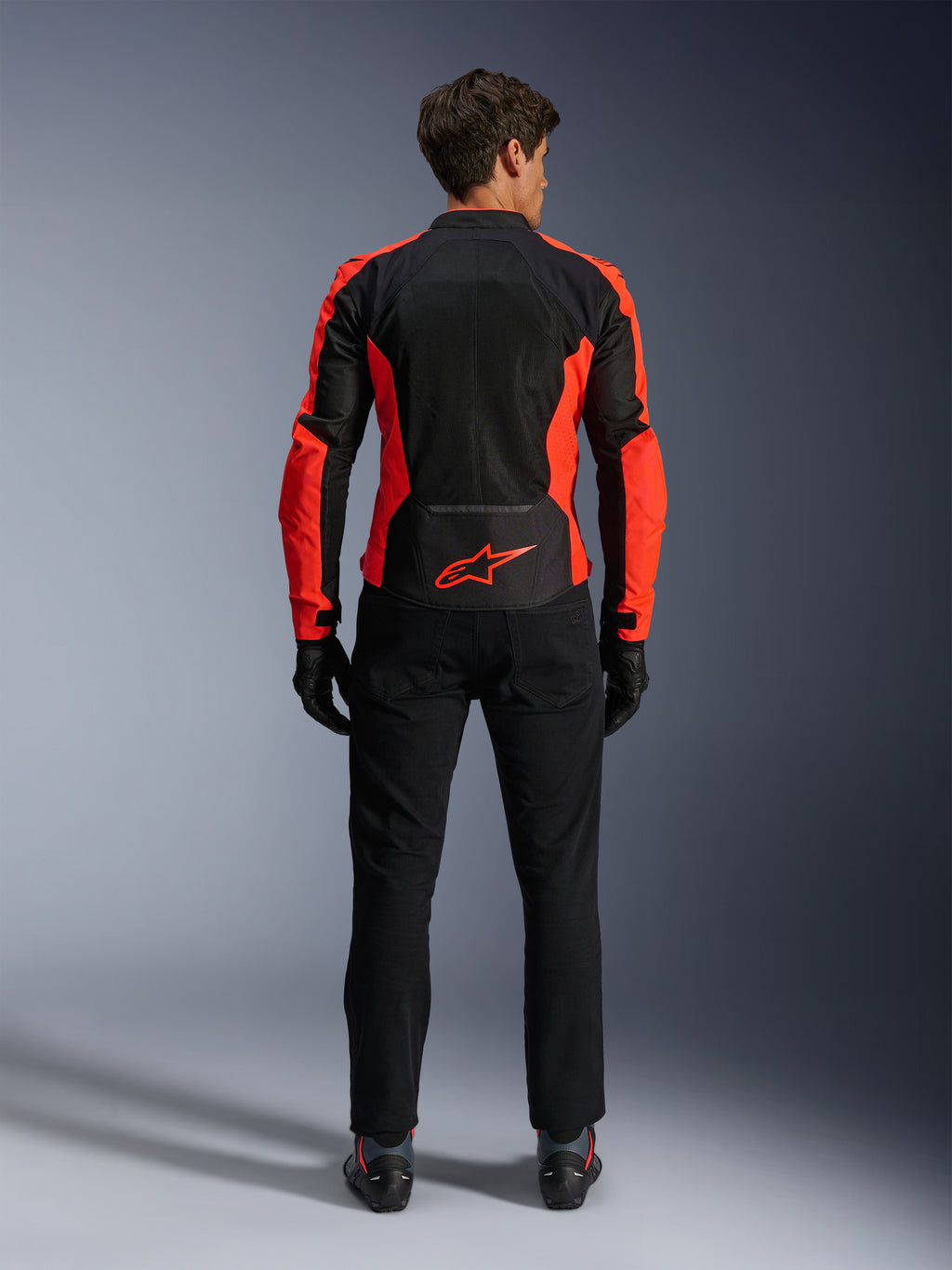 Casaco Alpinestars Viper Air V4, Vermelho Fluo e Preto, vista traseira realçando grandes painéis de malha técnica e pormenores laterais em vermelho fluorescente, logótipo Alpinestars vermelho na zona lombar, usado com calças e luvas de condução pretas