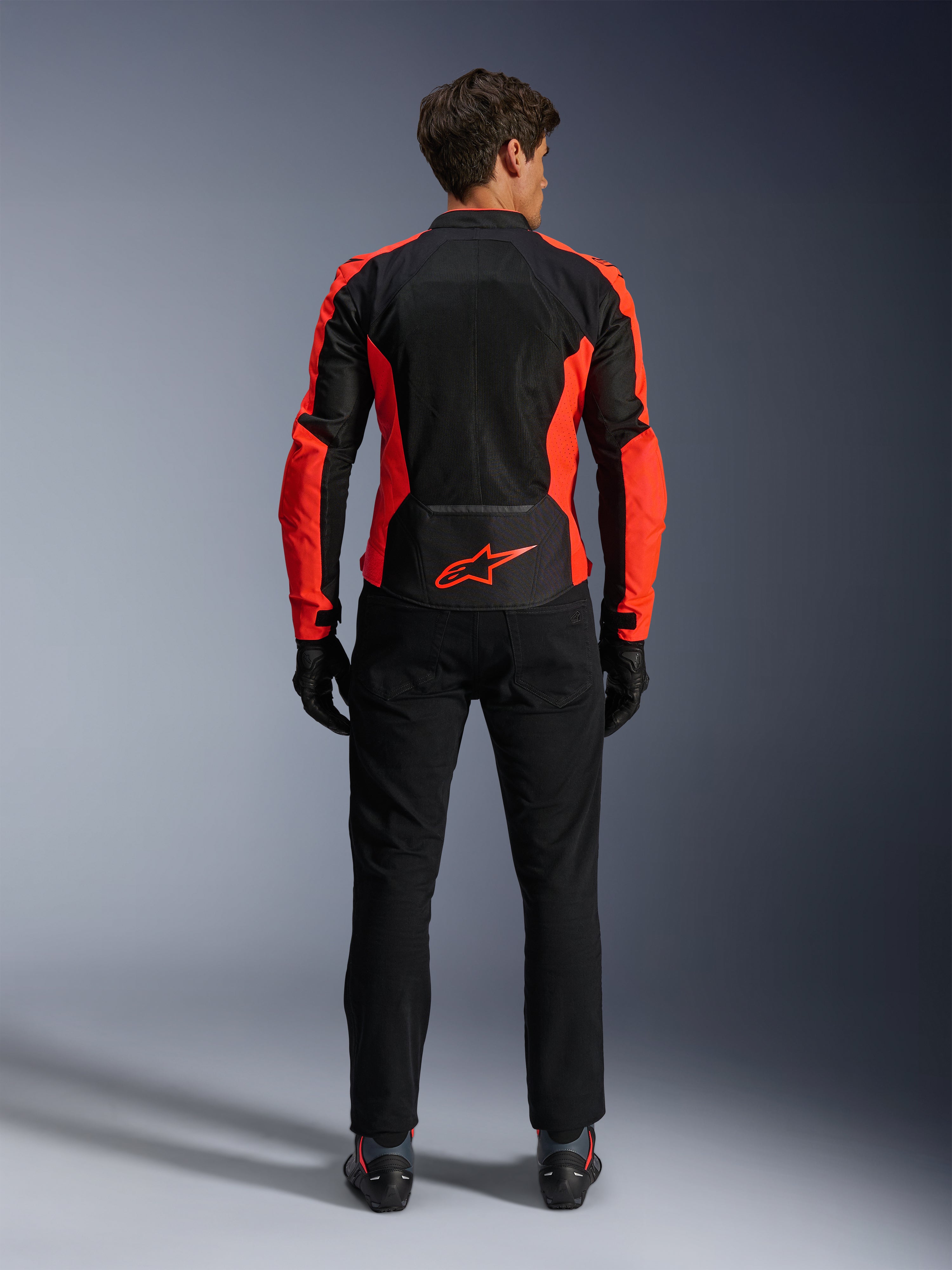 Casaco Alpinestars Viper Air V4, Vermelho Fluo e Preto, vista traseira realçando grandes painéis de malha técnica e pormenores laterais em vermelho fluorescente, logótipo Alpinestars vermelho na zona lombar, usado com calças e luvas de condução pretas
