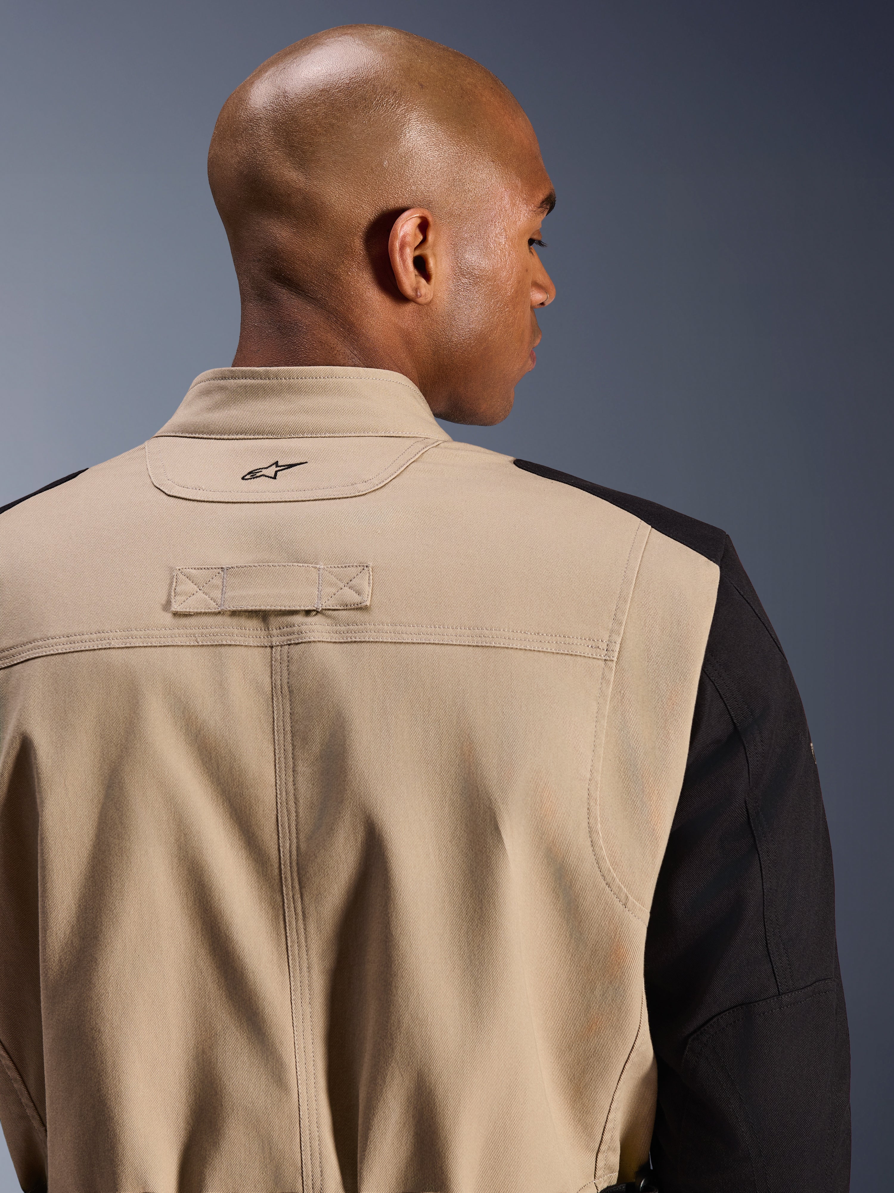 Alpinestars Dice Jacket, casaco de motociclismo urbano, bege e preto, detalhe em grande plano da gola traseira e do ombro, com logótipo bordado, construção robusta em sarja de policotão, estilo workwear pronto para a rua