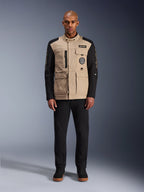 Casaco Alpinestars Dice, casaco de motociclismo urbano, corpo bege alumínio com mangas pretas, silhueta inspirada em vestuário de trabalho com quatro bolsos utilitários frontais, usado com calças pretas e sapatilhas de cano alto pretas, equipamento de condução robusto e urbano