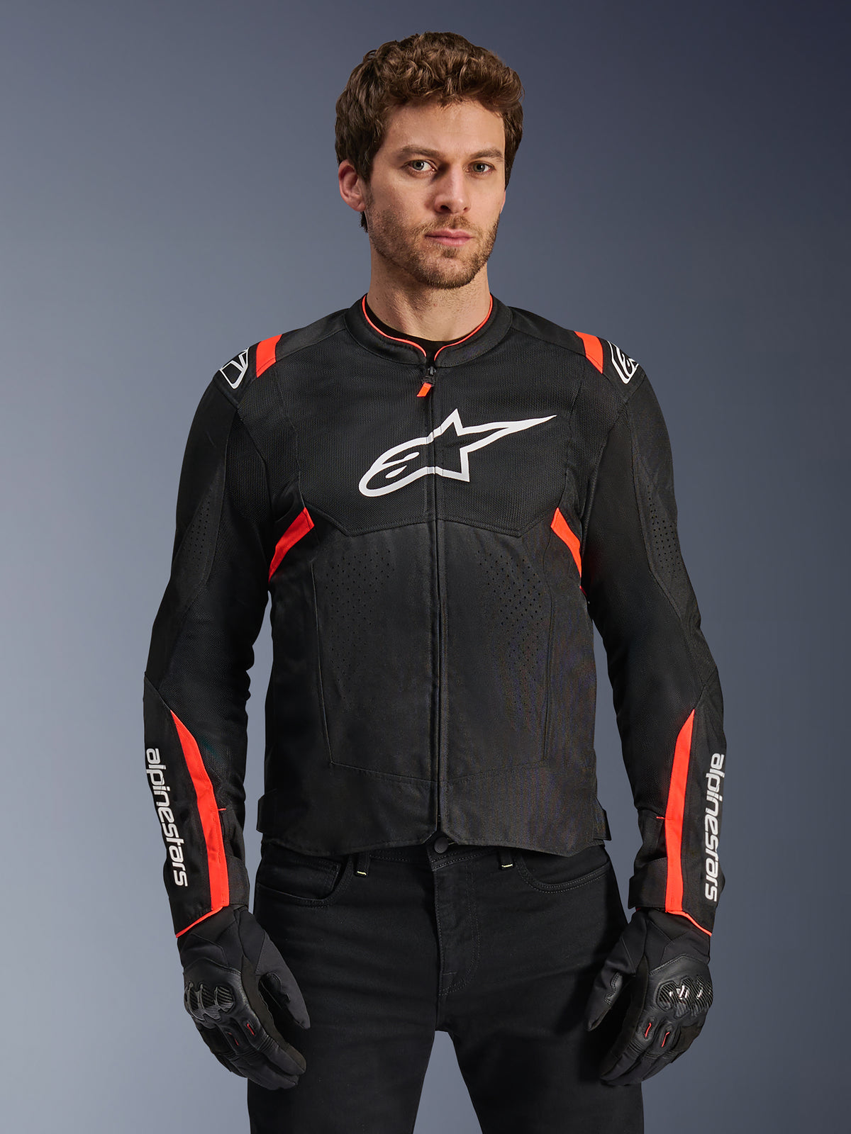 Alpinestars T-SPS Air V2, casaco de moto ventilado para homem, preto e vermelho fluo, com painéis em malha técnica para fluxo de ar, modelo a usar o casaco com luvas pretas.