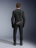 Casaco Alpinestars T-SPS Air v2 em Preto e Vermelho Fluo, vista traseira com grandes painéis de ventilação em malha e logótipo Alpinestars branco na zona lombar, usado com calças e botas de motociclismo pretas