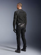 Casaco Alpinestars T-Sps Air V2, casaco de motociclismo em tecido, preto, vista traseira mostrando um grande painel de ventilação em malha e o logótipo Alpinestars branco na parte inferior das costas, combinado com calças e luvas de condução pretas para um visual urbano e desportivo.