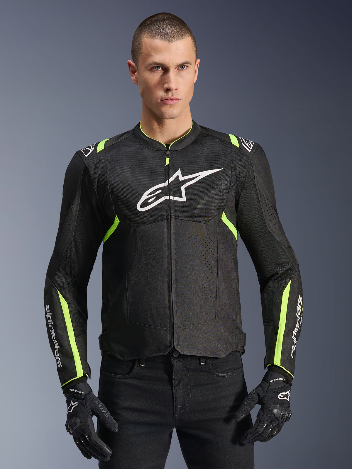 Casaco Alpinestars T-Sps Air V2 em preto e amarelo néon, modelo masculino a usar o casaco têxtil ventilado com painéis de malha e logótipo branco no peito, combinado com luvas de condução pretas, equipamento urbano de motociclismo