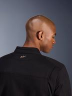 Alpinestars Bruiser Jacket, preto, pormenor das costas da gola e da parte superior dos ombros, com um pequeno logótipo Alpinestars bordado em bege no pescoço, casaco de motociclismo urbano com estética de vestuário de trabalho