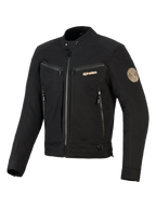 Alpinestars Bruiser Jacket, casaco de motociclismo urbano preto, inclui bolsos com fecho no peito e para as mãos, logótipo em tons dourados e patch de ombro em espiral Oscar, design têxtil inspirado em vestuário de trabalho.