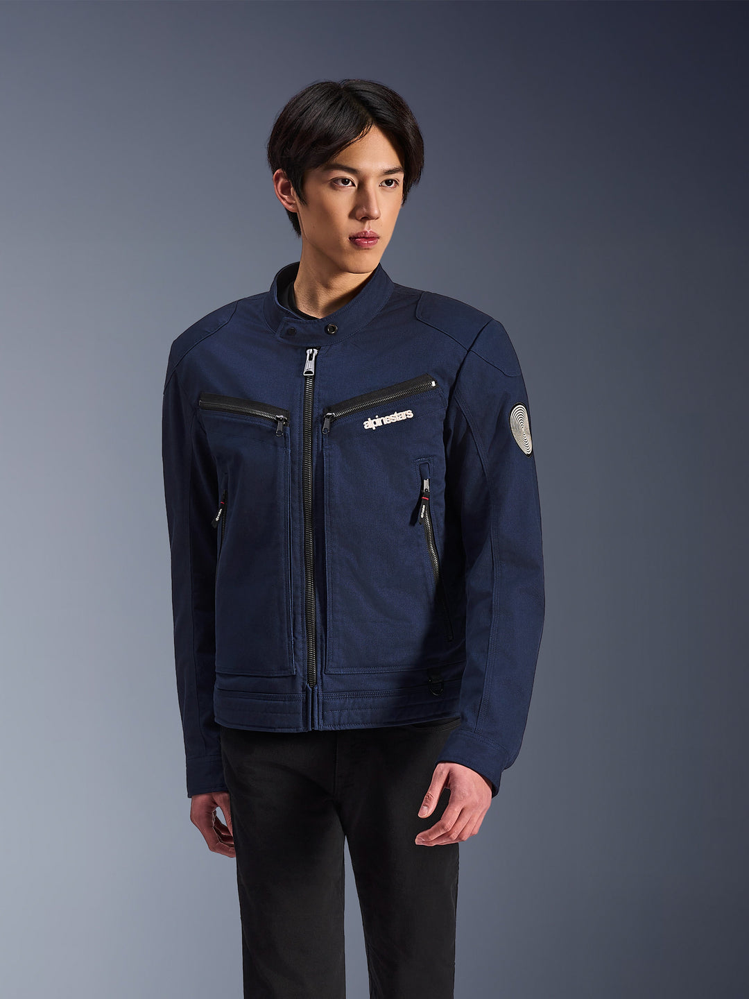 Alpinestars Bruiser Jacket, casaco casual de moto, azul-escuro com fechos pretos, logótipo no peito, patch redondo na manga, estilo urbano premium