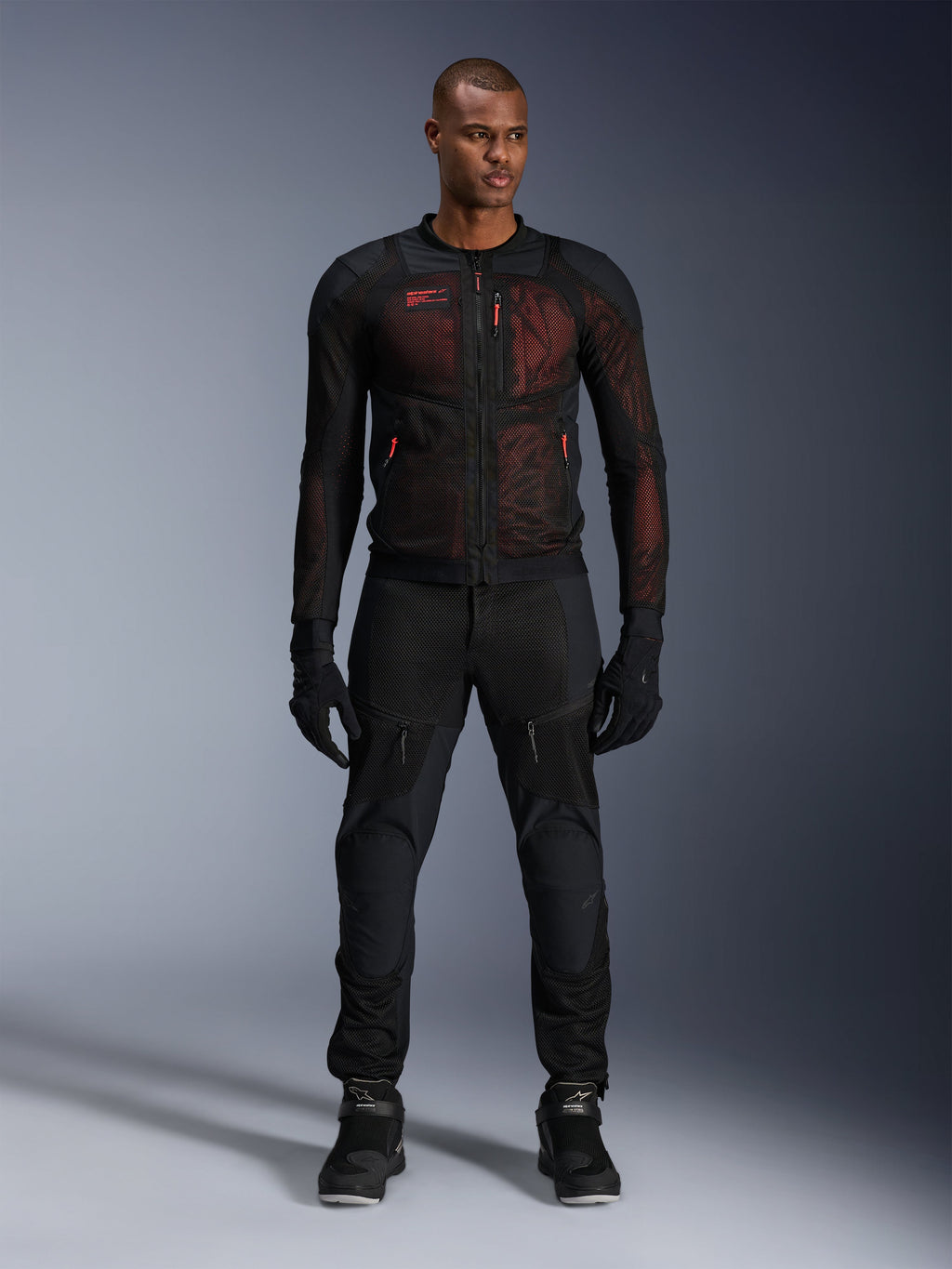 Casaco Alpinestars Troop-Air Pro, casaco de ar técnico blindado, Preto e Vermelho Fluo, usado por modelo masculino com calças e luvas de condução a condizer, com painéis de malha de alto fluxo e detalhes em vermelho, equipamento urbano para motociclista