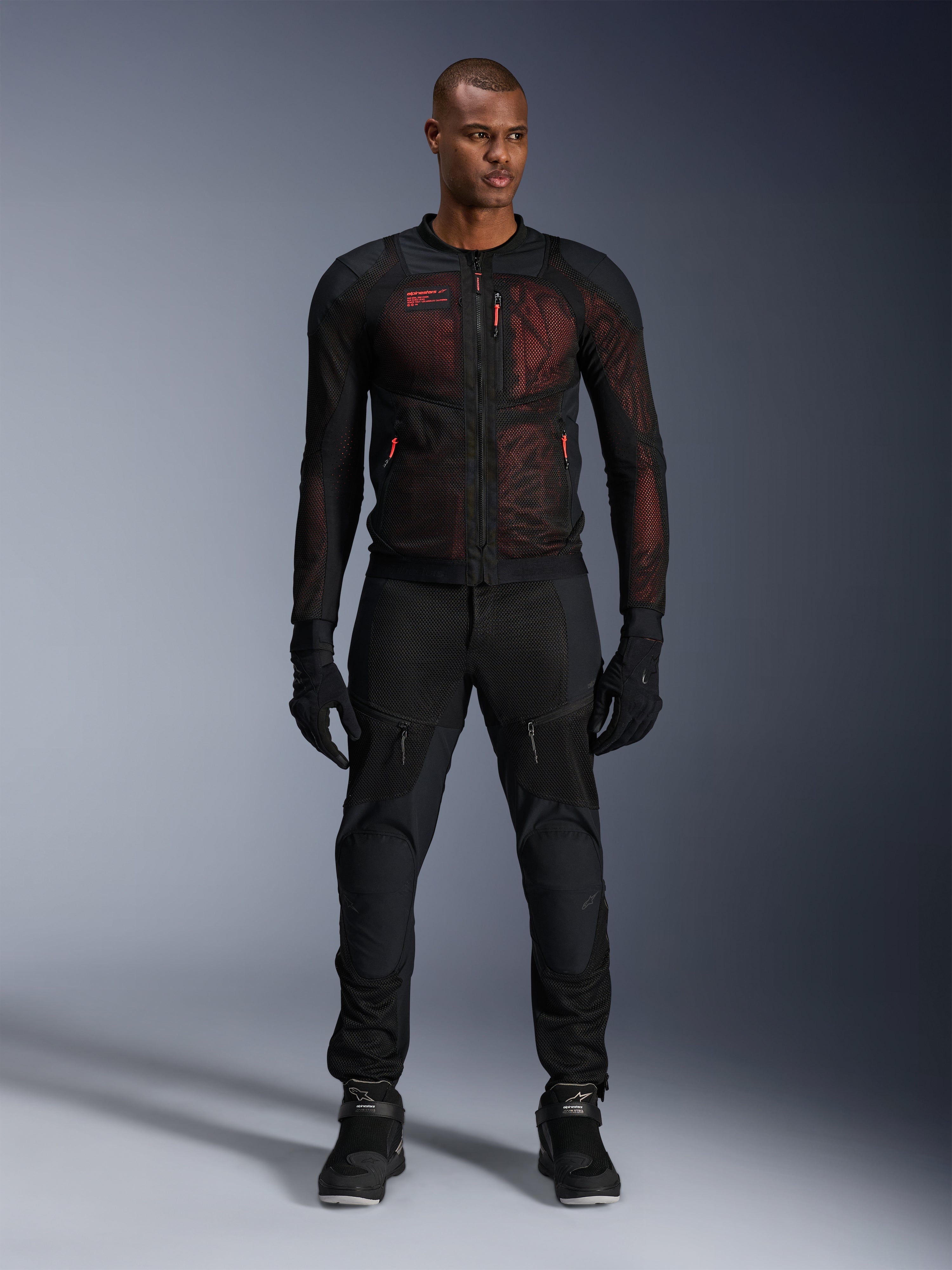 Casaco Alpinestars Troop-Air Pro, casaco de ar técnico blindado, Preto e Vermelho Fluo, usado por modelo masculino com calças e luvas de condução a condizer, com painéis de malha de alto fluxo e detalhes em vermelho, equipamento urbano para motociclista