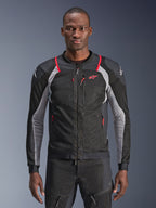 Alpinestars Troop-Air Pro Jacket, preto, cinzento ash e vermelho brilhante, usado por um modelo, casaco de malha para motociclismo com painéis de ventilação perfurados, com bolsos de fecho vermelhos e logótipos brancos nos ombros, equipamento técnico de proteção para motociclismo