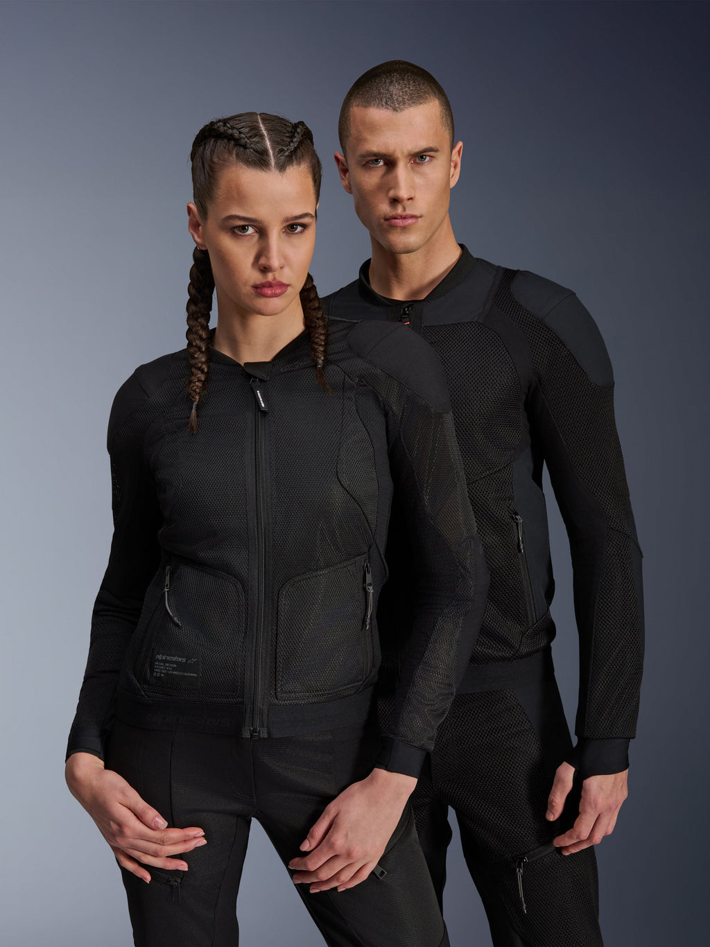 Casaco Alpinestars Troop-Air Pro, casacos técnicos blindados pretos vestidos por modelos masculino e feminino, com painéis de malha respirável e proteção integrada, equipamento de motociclismo urbano concebido para condução em climas quentes.