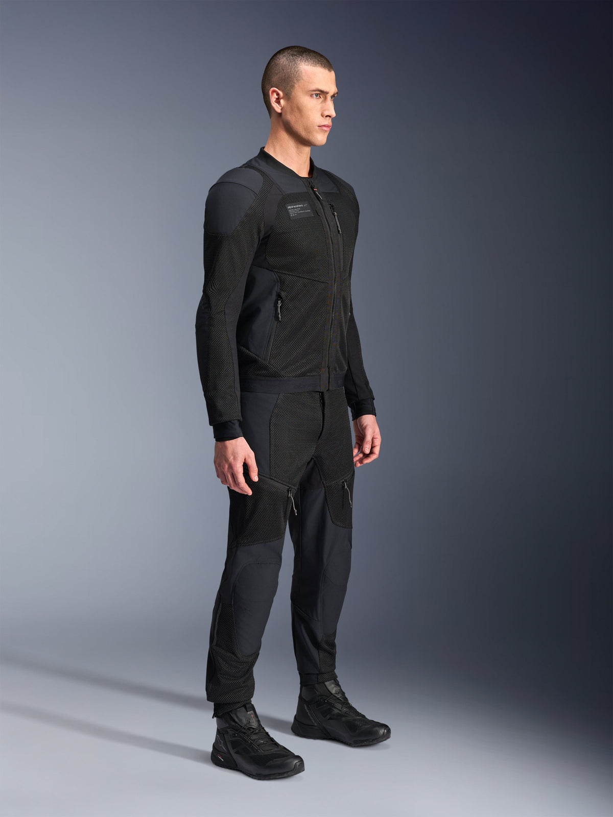 Casaco Alpinestars Troop-Air Pro, casaco de ar blindado técnico, preto, usado por modelo com calças e botas de motociclismo pretas a condizer, com estrutura de malha tecnológica 2D avançada e painéis de ventilação respiráveis, equipamento de condução urbano contemporâneo.