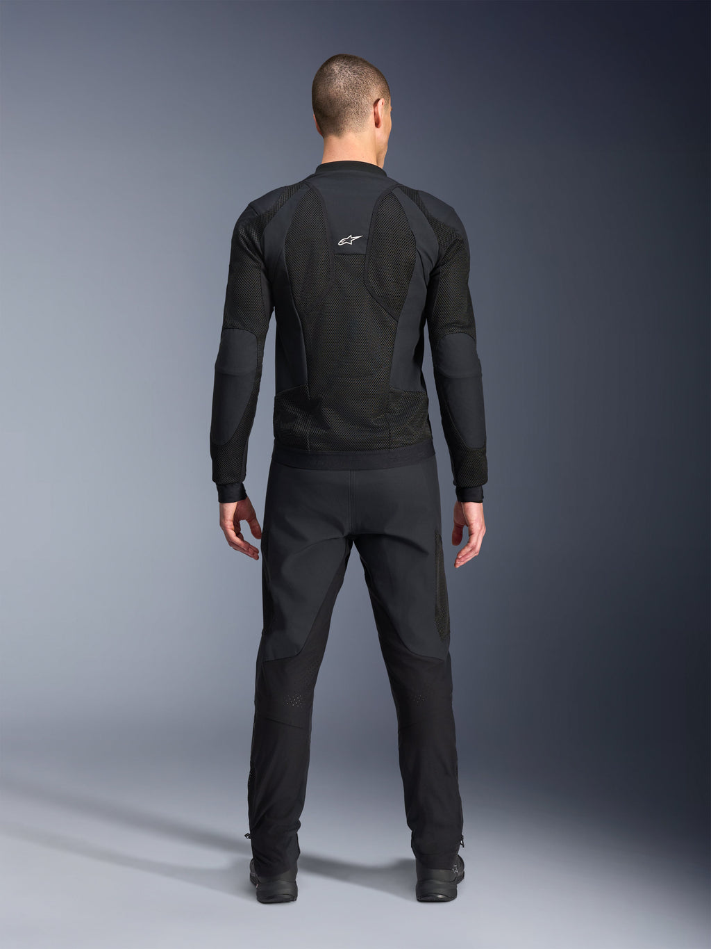 Casaco Alpinestars Troop-Air Pro, vista traseira, preto, casaco de motociclismo técnico com ventilação com grandes painéis de ventilação em malha e logótipo branco da Alpinestars, combinado com calças pretas, equipamento de condução urbano contemporâneo