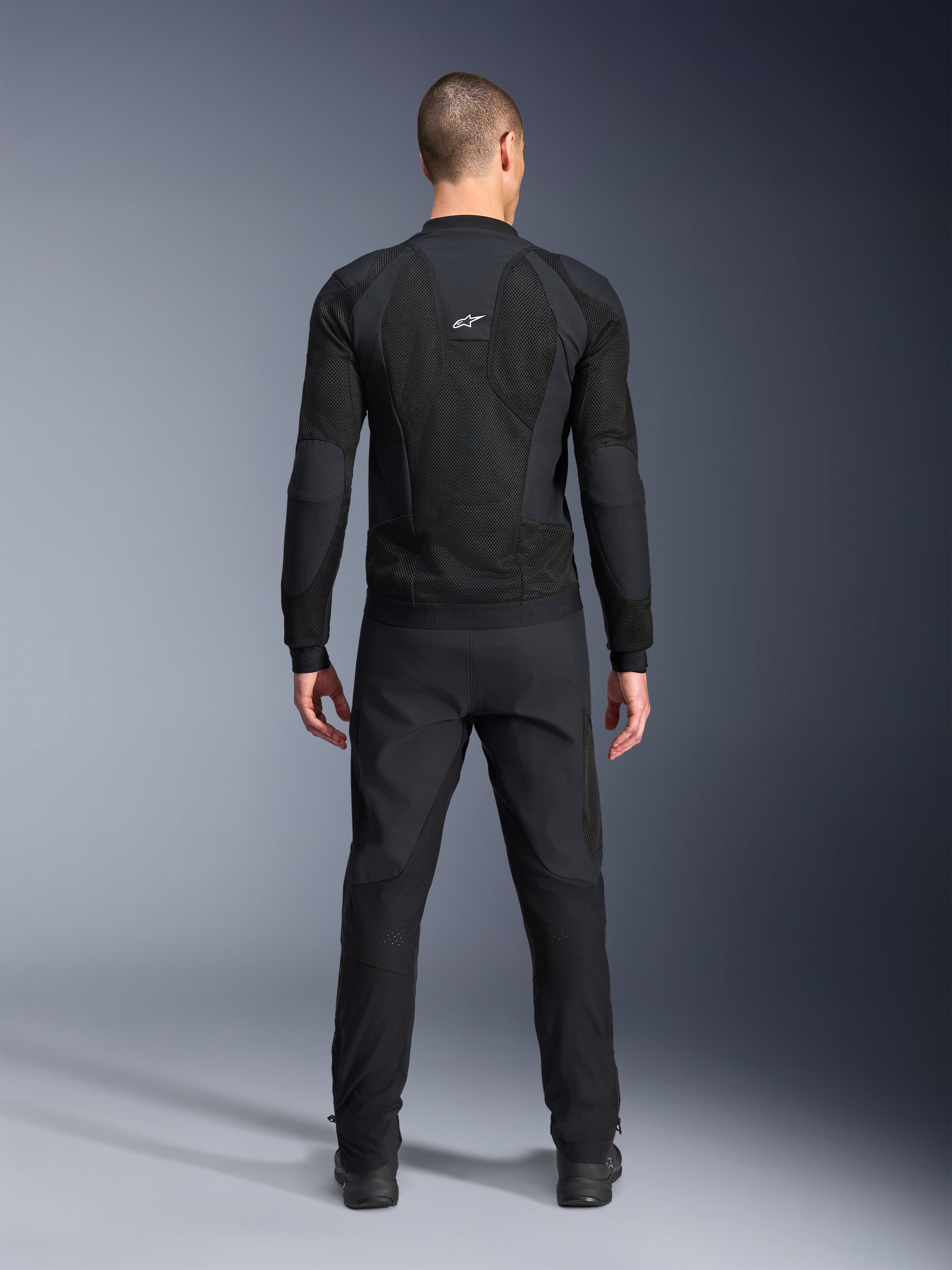 Casaco Alpinestars Troop-Air Pro, vista traseira, preto, casaco de motociclismo técnico com ventilação com grandes painéis de ventilação em malha e logótipo branco da Alpinestars, combinado com calças pretas, equipamento de condução urbano contemporâneo