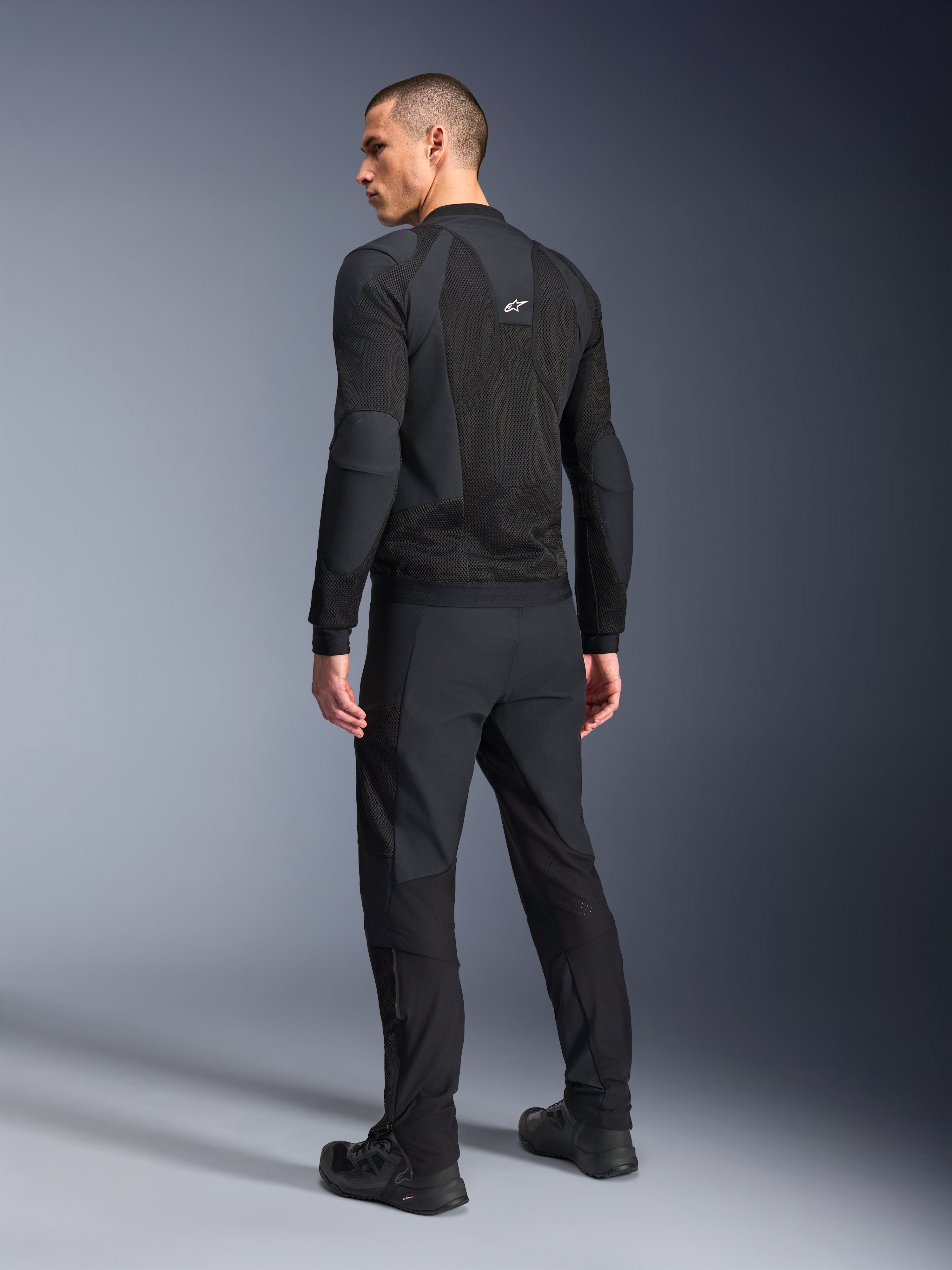Casaco Alpinestars Troop-Air Pro, preto, casaco de ar técnico com proteções visto de costas, com amplos painéis de malha para fluxo de ar, combinado com calças técnicas e sapatos pretos a condizer