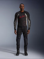 Male model wearing the Alpinestars Troop-Air Jacket in Black Ash Gray and Bright Red, technical mesh motorcycle jacket featuring a prominent red chest logo, styled with black motorcycle pants and boots, urban road riding apparel