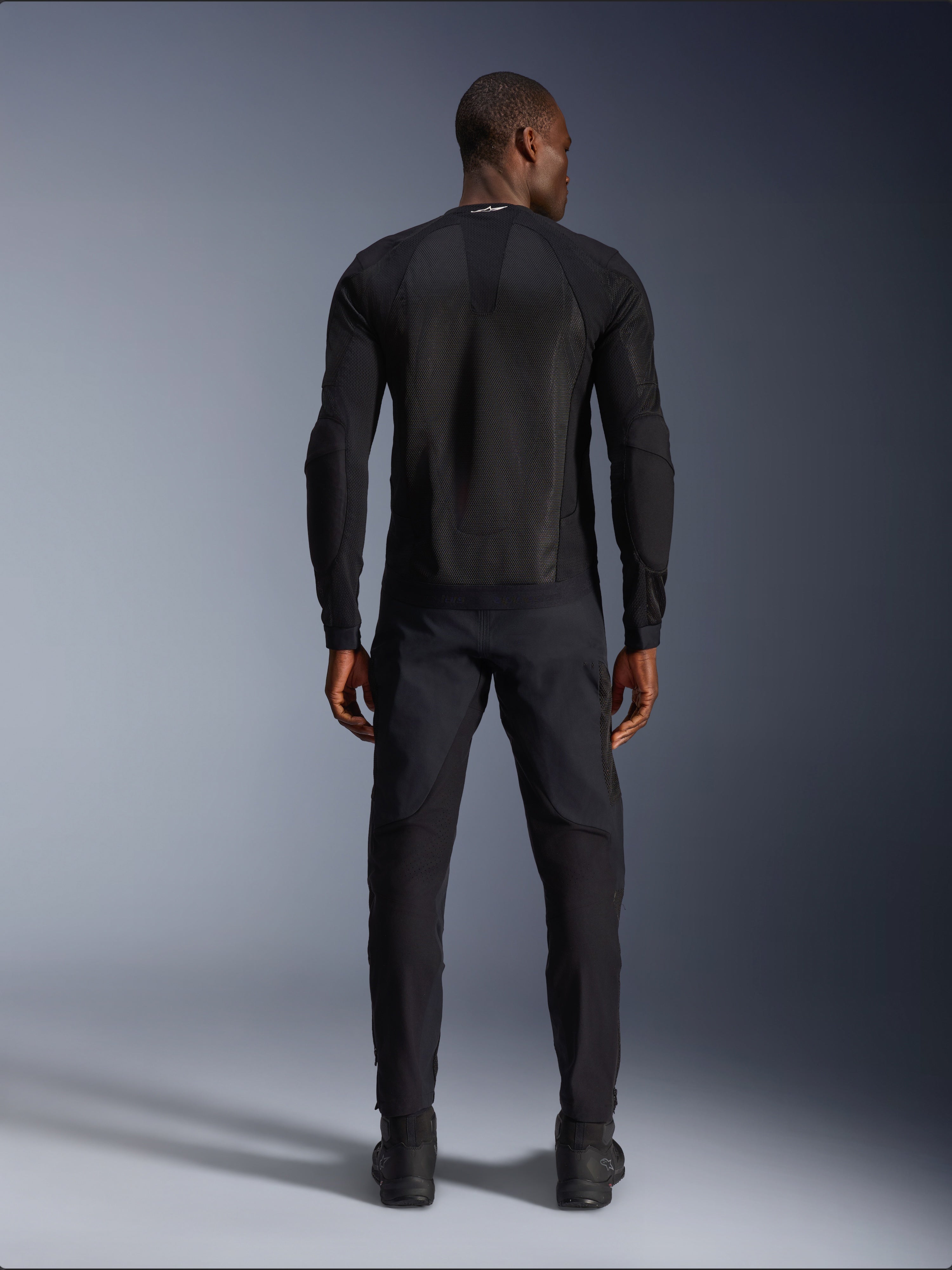 Casaco Alpinestars Troop-Air em Black Black, vista traseira mostrando o painel das costas em malha técnica e construção ventilada, combinado com calças e botas de motociclismo pretas a condizer.