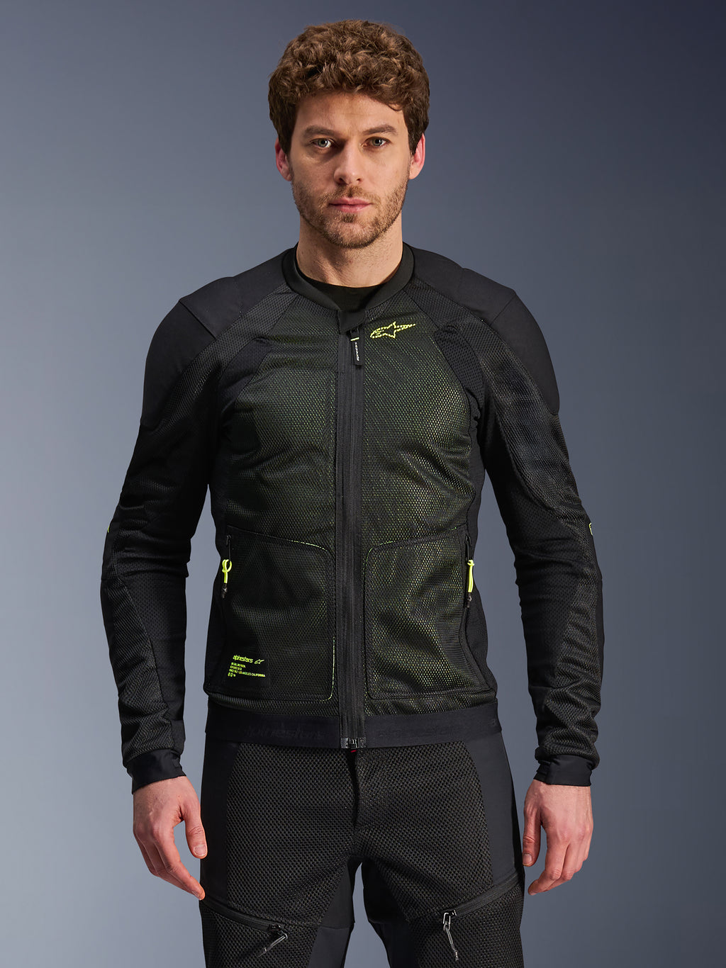 Casaco Alpinestars Troop-Air, preto e amarelo néon, usado por modelo masculino, com construção em malha leve, fechos e logótipos amarelo néon, casaco de motociclismo técnico ventilado para condução urbana
