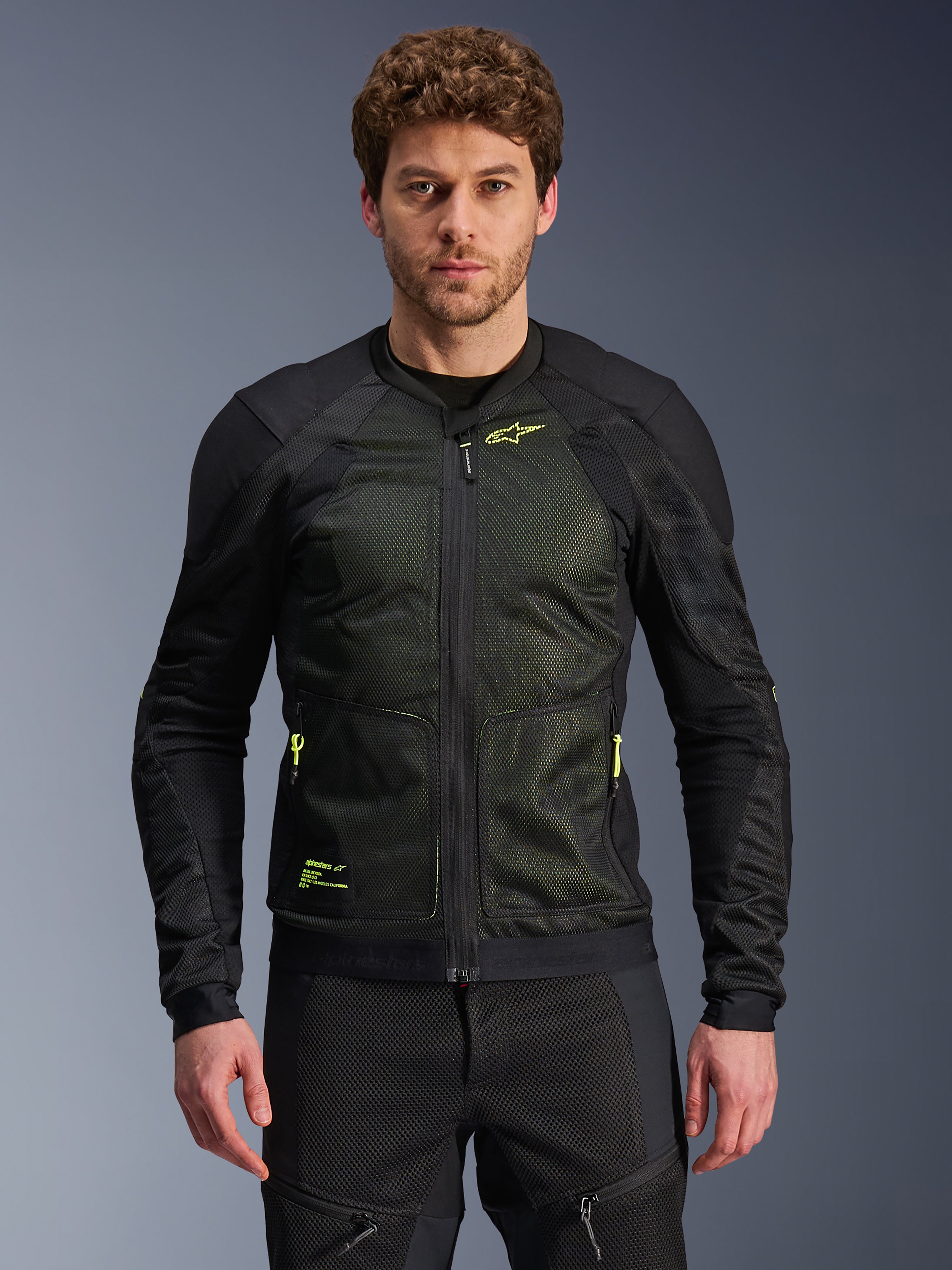 Casaco Alpinestars Troop-Air, preto e amarelo néon, usado por modelo masculino, com construção em malha leve, fechos e logótipos amarelo néon, casaco de motociclismo técnico ventilado para condução urbana