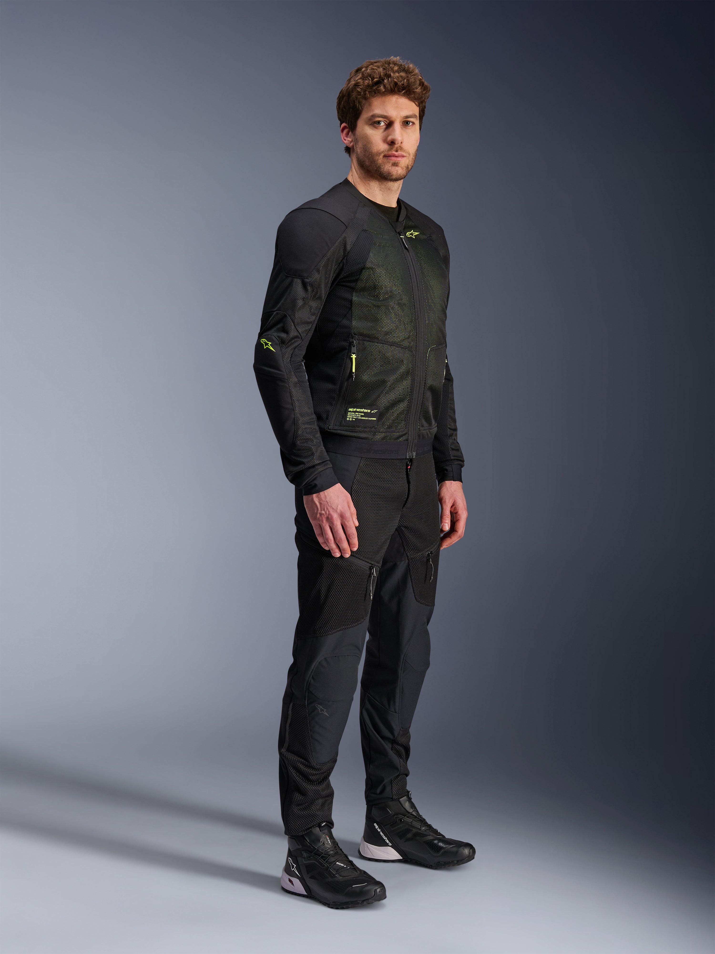 Casaco Alpinestars Troop-Air, casaco de malha para motociclismo, preto e amarelo fluo, vestido por um modelo com calças pretas e sapatilhas de condução a condizer, apresenta construção em malha de elevado fluxo de ar com detalhes em amarelo fluorescente no peito e nas mangas, design técnico leve para condução em estrada