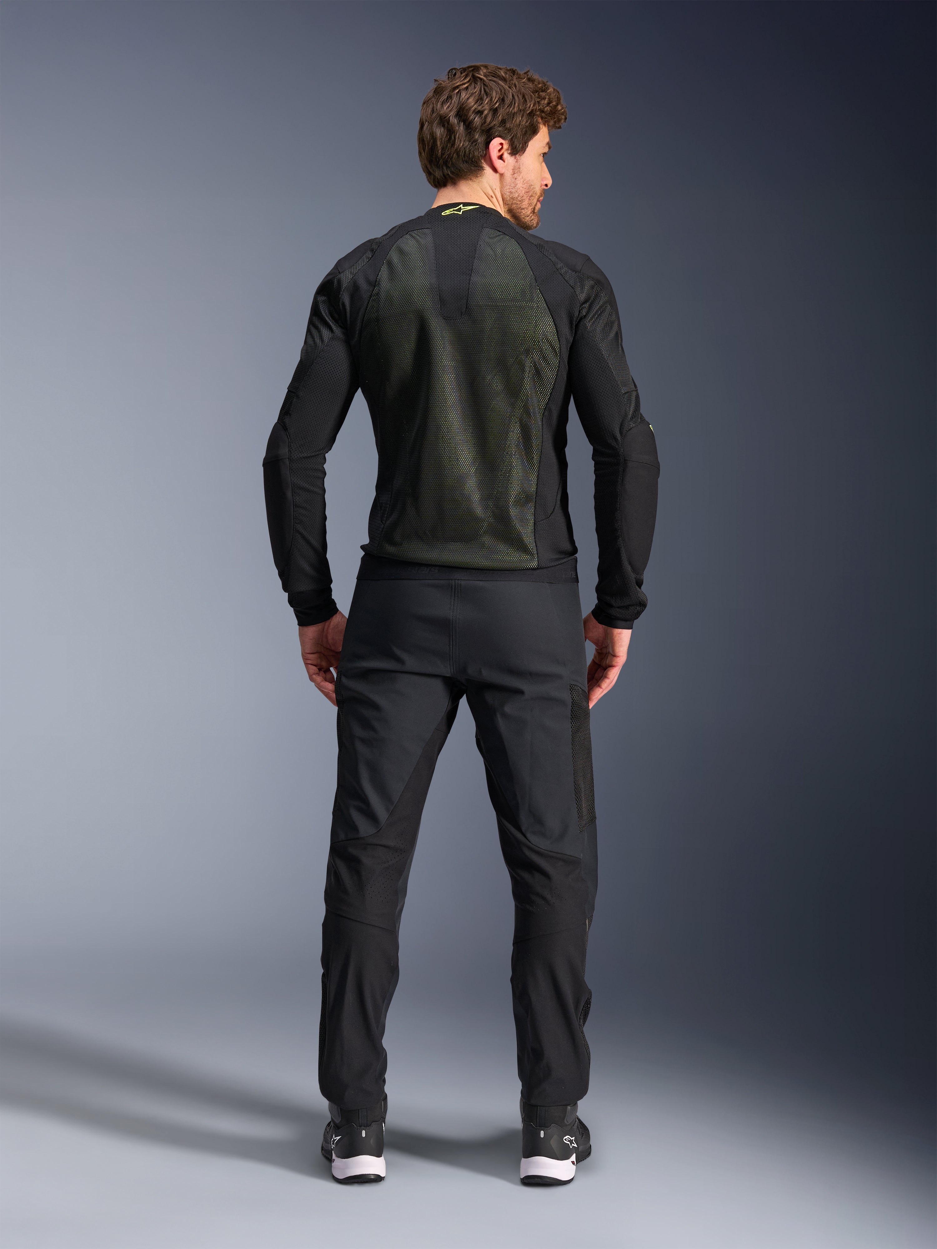 Alpinestars Troop-Air Jacket, Preto Amarelo Fluo, vista traseira num modelo, com um grande painel traseiro em malha técnica 2D para ventilação, casaco técnico de motociclismo usado com calças e botas pretas, estilo urbano de motociclismo