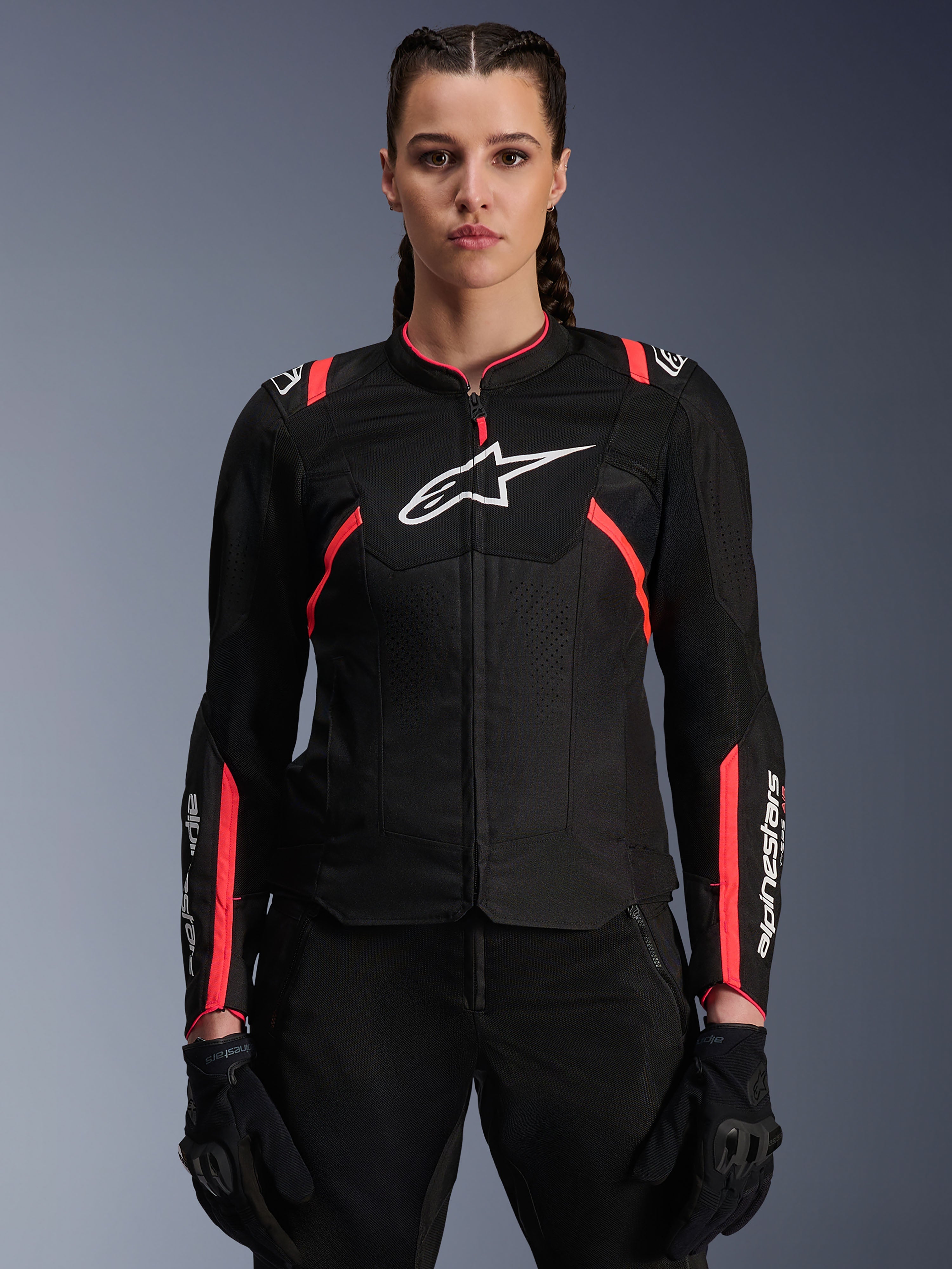 Casaco Alpinestars Stella T-Sps Air V2 para mulher, preto e rosa diva, casaco de motociclismo têxtil com painéis de malha respirável e pormenores em rosa, logótipo Alpinestars branco no peito, usado por uma modelo feminina com calças e luvas de condução pretas