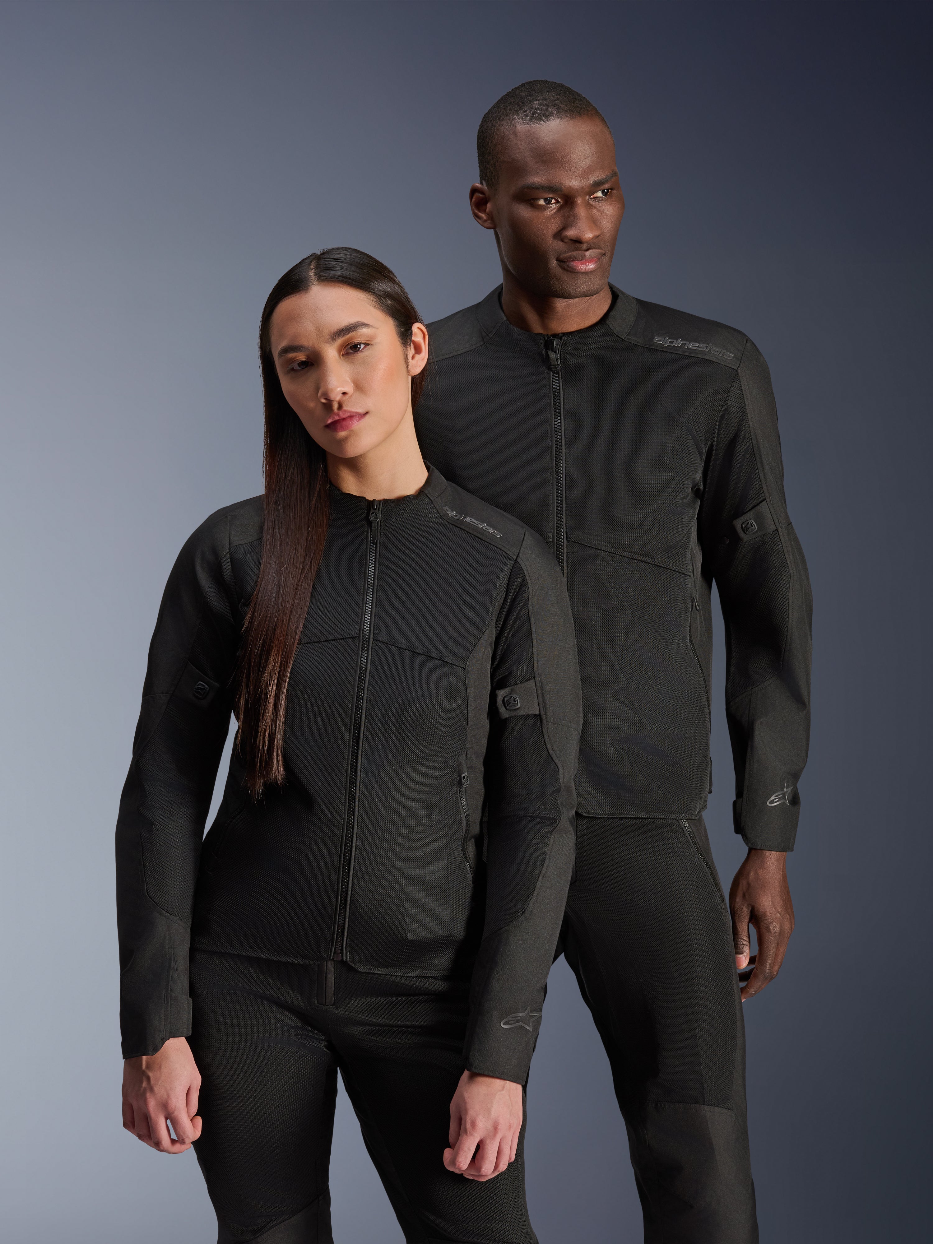 Um homem e uma mulher a usar os casacos Alpinestars C-1 Air e Stella C-1 Air, casacos de motociclismo urbanos em têxtil preto com painéis de malha para ventilação, combinados com calças de condução pretas para um visual limpo e contemporâneo.