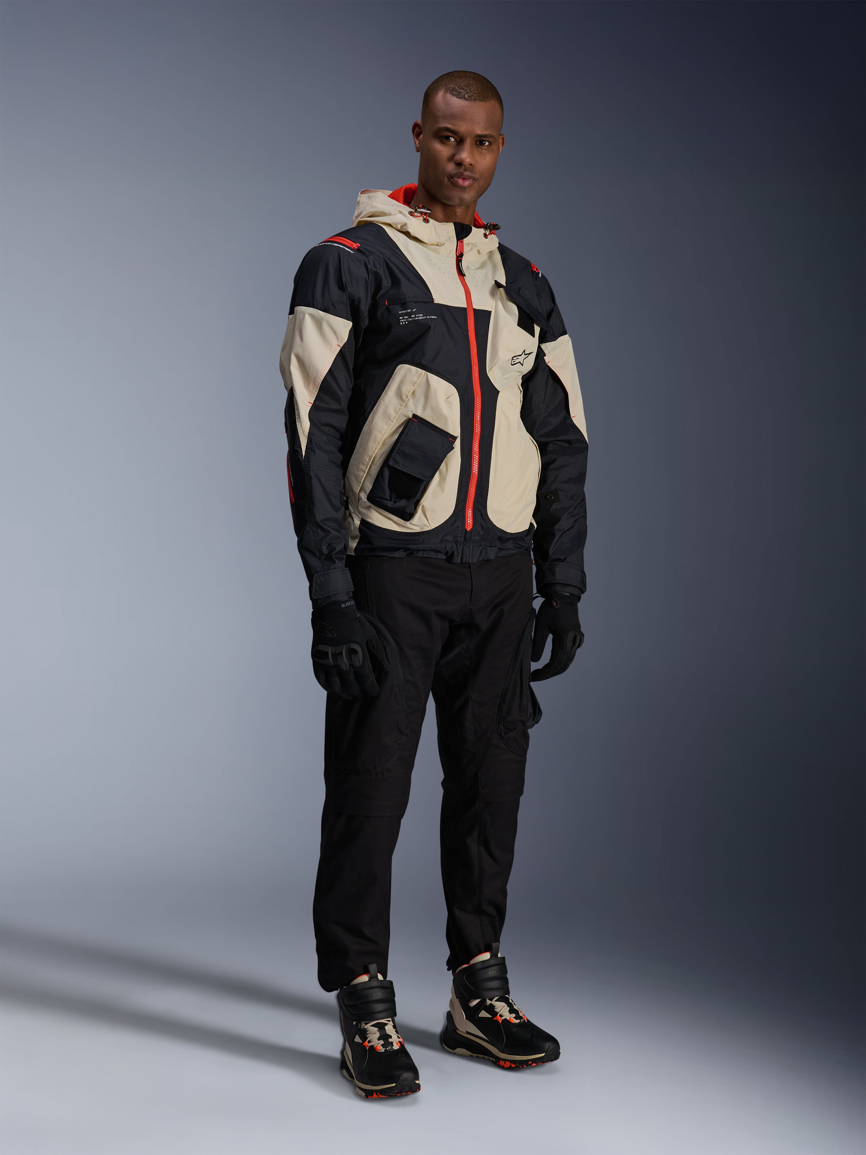 Homem com equipamento completo de motociclismo urbano Alpinestars, incluindo sapatos Speedstreet em Black Almond Hot Orange e casaco Mogress Air em preto e creme, calças e luvas pretas coordenadas, conjunto de proteção inspirado em streetwear para condução urbana