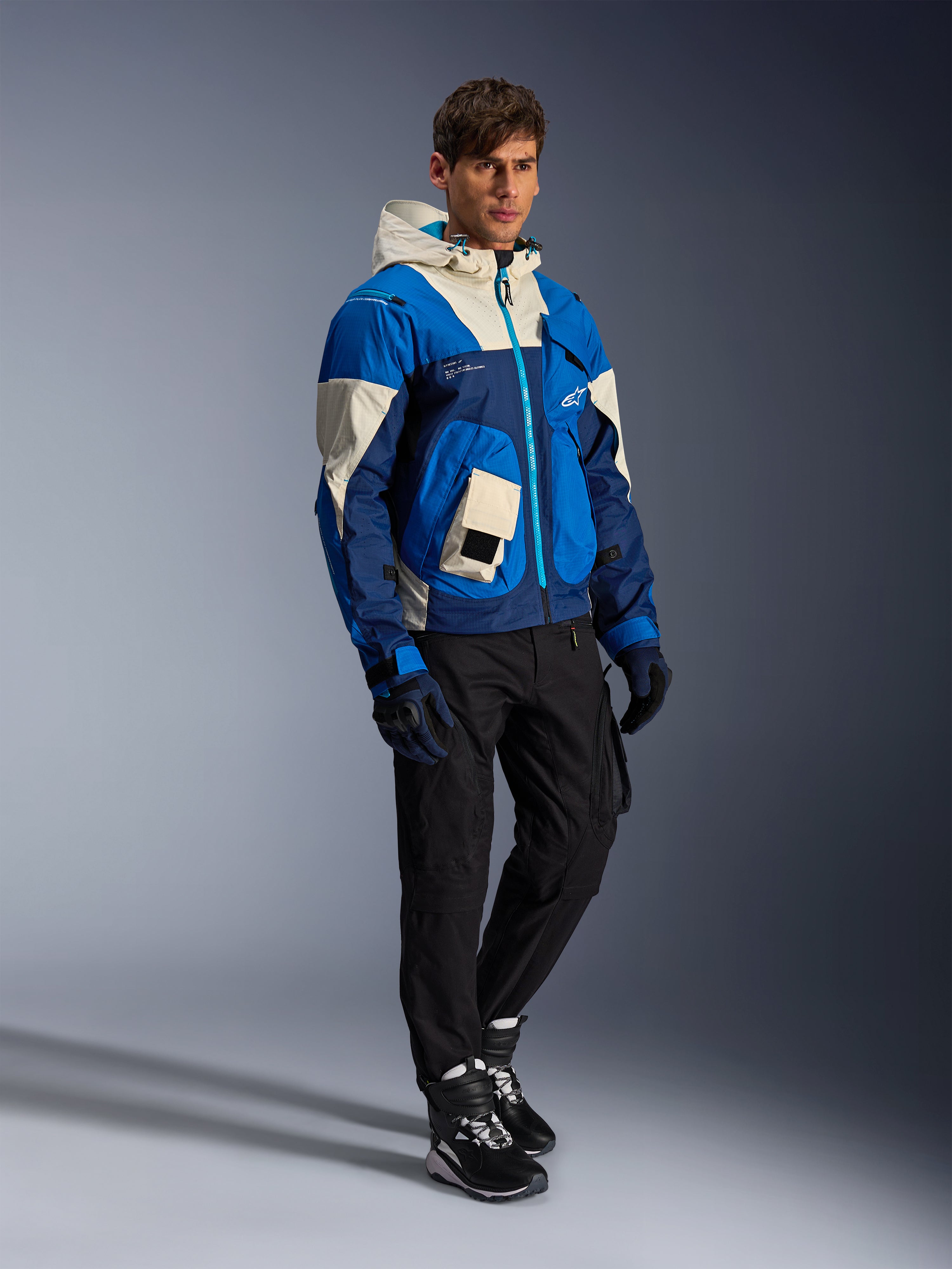 Casaco Alpinestars Mogress Air, casaco de motociclismo urbano, cor Blue Almond com painéis creme e azul-marinho, com capuz e bolsos utilitários, usado com calças de condução pretas, luvas e botas, equipamento de proteção contemporâneo inspirado em streetwear.