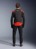 Casaco Alpinestars T-Stunt Air, preto com detalhes em vermelho fluo e vermelho escuro, vista traseira no modelo, combinado com calças e botas de condução pretas, com logótipo Alpinestars proeminente no painel inferior traseiro, design modular com construção em malha para ventilação.