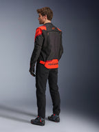 Homem a usar o Casaco Alpinestars T-Stunt Air visto de costas, em Preto Vermelho Fluo e Vermelho Escuro, casaco de motociclismo têxtil com painéis de malha e design de corte desportivo, com o logótipo Alpinestars em destaque na parte inferior das costas, combinado com calças pretas e botas de condução.