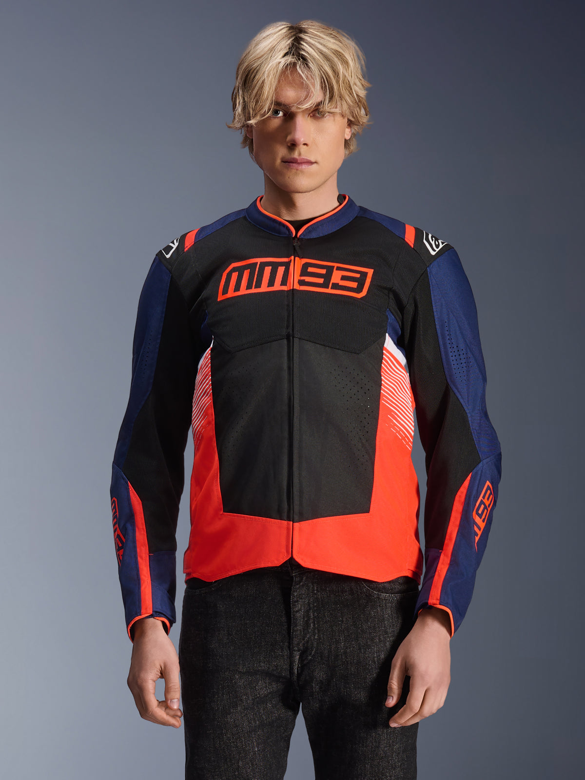 Casaco Alpinestars MM93 T-SPS Air V2, casaco de motociclismo têxtil, azul-marinho, preto e vermelho fluorescente, vestido por uma pessoa, com marca MM93 em destaque no peito, painéis de malha para ventilação e design moderno em blocos de cor