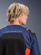 Alpinestars MM93 T-SPS Air V2 Jacket, Blue Navy and Black with Red Fluo accents, close-up of the upper back featuring 'MARC MARQUEZ' branding, breathable mesh panels and perforated textile construction, worn by a blonde model.