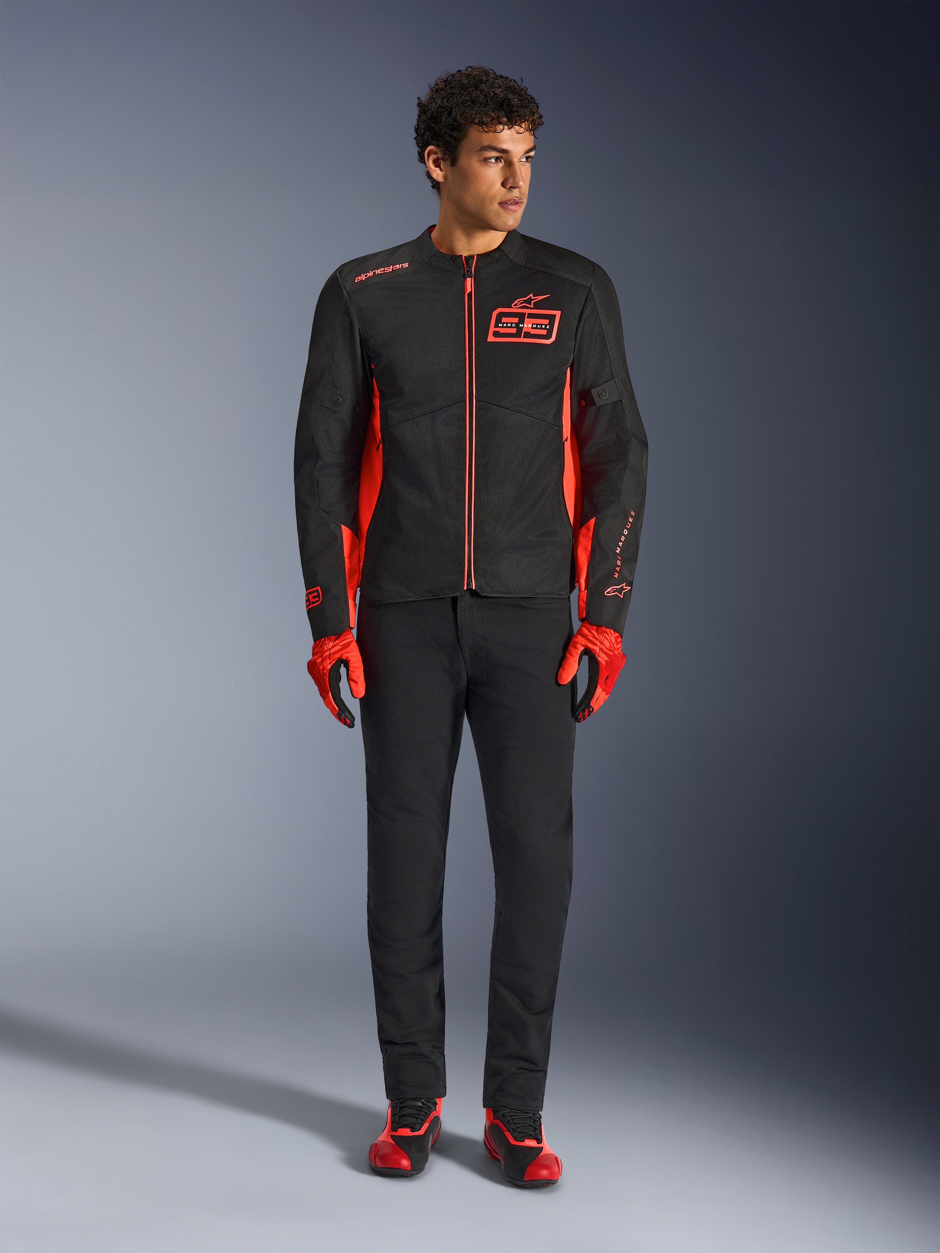 Alpinestars MM93 C-1 Air Jacket, casaco de motociclismo, preto e vermelho fluorescente, com a marca Marc Marquez e o logótipo 93, usado por um modelo com luvas vermelhas a condizer e calças pretas, construção leve em têxtil e malha para condução urbana