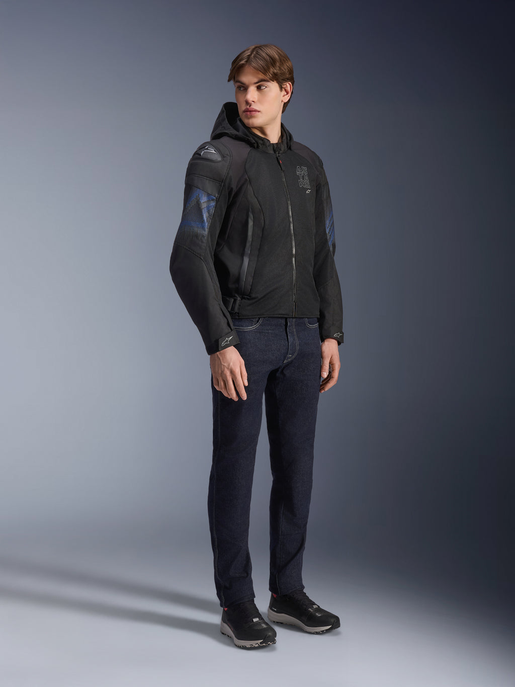 Alpinestars Zaca Air Venom WP Jacket, casaco de motociclismo têxtil em preto e azul elétrico, usado por modelo com calças de ganga escuras e sapatilhas pretas, inclui capuz removível, painéis de ventilação em malha e deslizadores de ombro DFS Lite, equipamento desportivo para todas as condições climatéricas