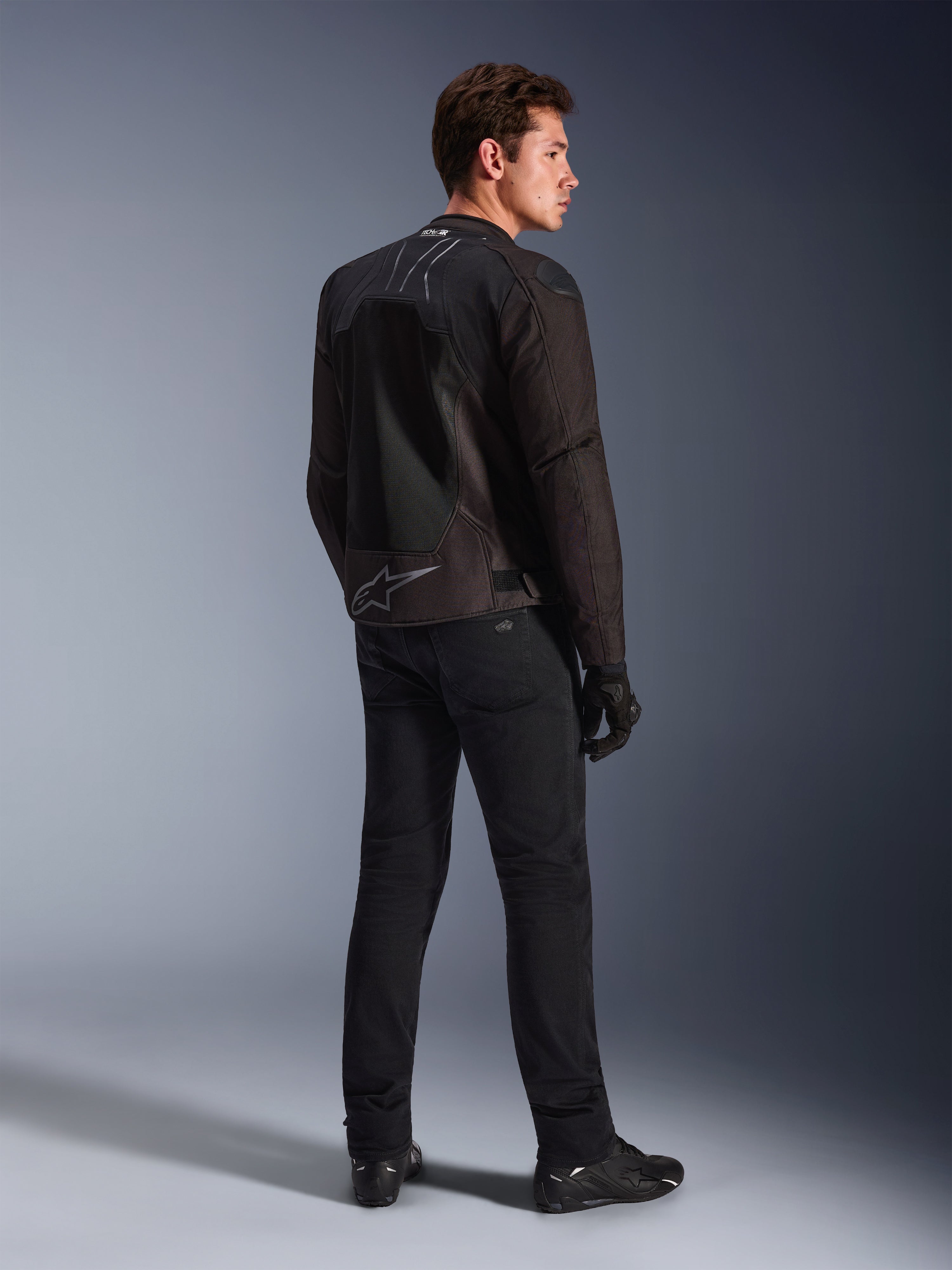 Casaco Alpinestars SMX Air em Preto Antracite, vista traseira no modelo, apresentando a marca Tech-Air® Ready no colarinho e o logótipo Astar na zona inferior das costas, usado com calças de condução pretas e sapatos pretos.