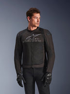 Casaco Alpinestars SMX Air em Black Anthracite, casaco de motociclismo em tecido com painéis de malha de alto fluxo, apresenta um grande logótipo e texto Alpinestars cinzento no peito, deslizadores de ombro DFS Lite, usado por um modelo com luvas de condução pretas, estilo de condução desportiva.