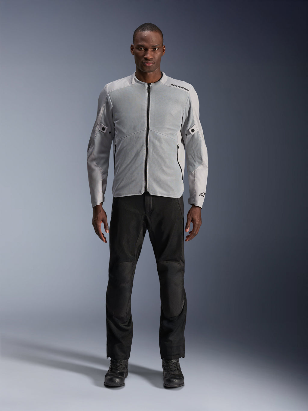 Casaco Alpinestars C-1 Air em prateado, casaco têxtil de motociclismo urbano para homem com painéis de malha ventilada, usado por um modelo com calças de condução pretas e botas pretas, estilo urbano contemporâneo