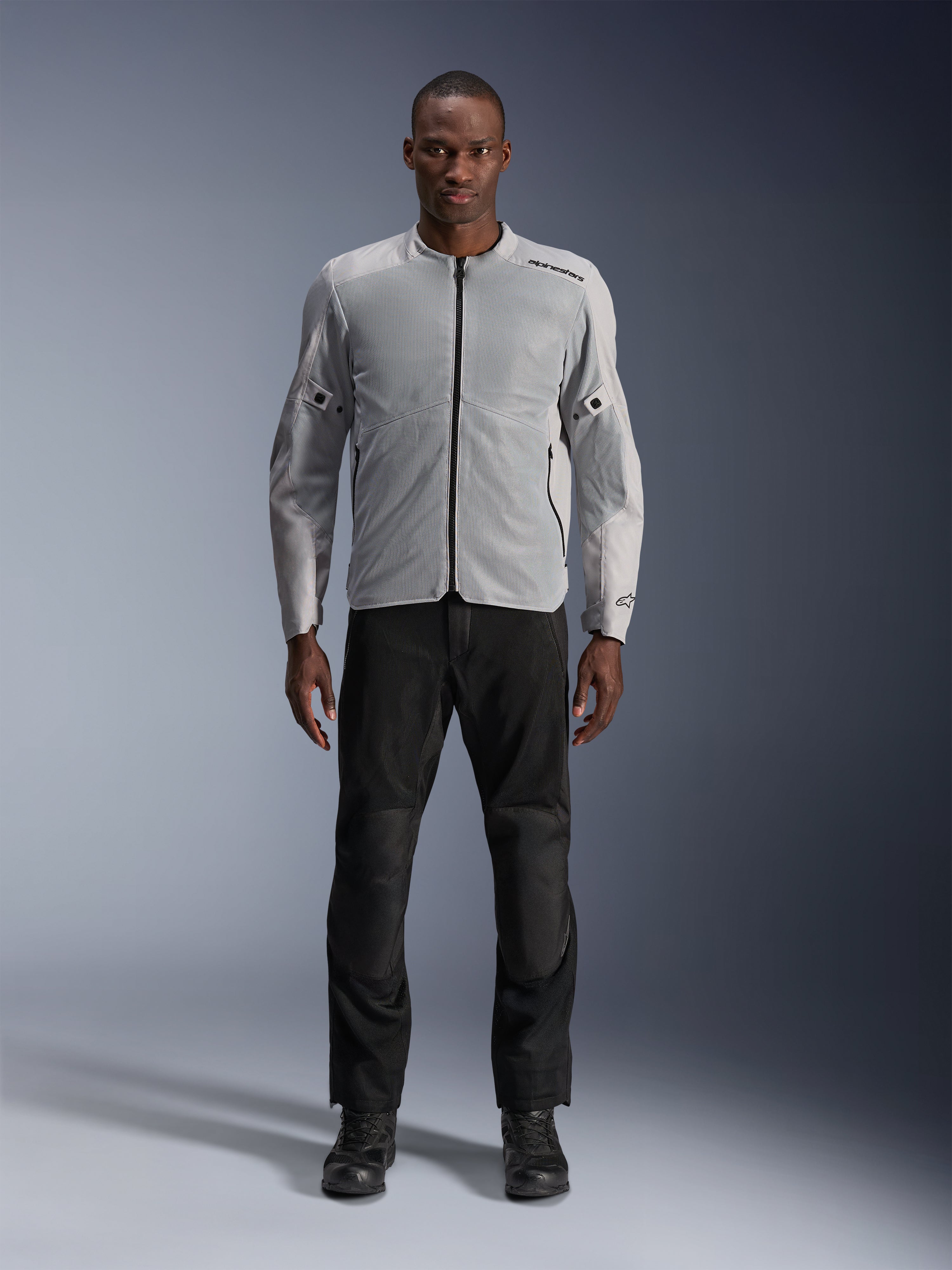 Casaco Alpinestars C-1 Air em prateado, casaco têxtil de motociclismo urbano para homem com painéis de malha ventilada, usado por um modelo com calças de condução pretas e botas pretas, estilo urbano contemporâneo