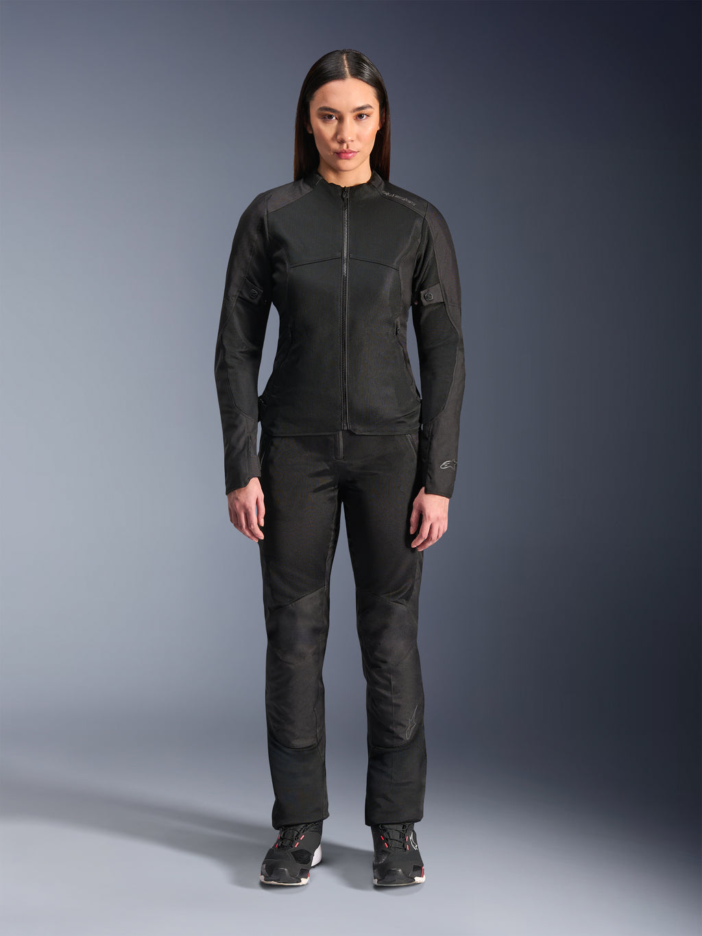 Woman wearing Alpinestars Stella C-1 Air Jacket in Black, paired with matching black textile motorcycle pants and riding shoes, featuring a sleek urban design with large mesh panels for airflow.