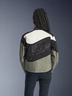 Woman from behind wearing the Alpinestars Stella Moshell Jacket, Black Gray and Off White urban motorcycle jacket, featuring a large white outlined logo on the back, paired with black pants, contemporary streetwear-inspired riding gear.